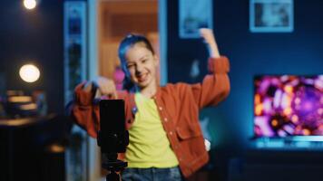 Kid vlogger recording trendy dance clip for social media using cellphone on tripod stabilizer, entertaining audiences. Gen z youngster recording viral content using mobile phone photo