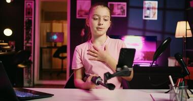 Zoom in shot on young child using smartphone attached to selfie stick to film content for her online fans, talking about gen Z topics. Happy kid recording vlog for family channel with cellphone camera photo