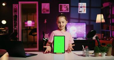 Smiling child in home studio presenting advertisement from sponsoring brand on green screen tablet. Little kid using chroma key device to present promotion from media partner to followers photo