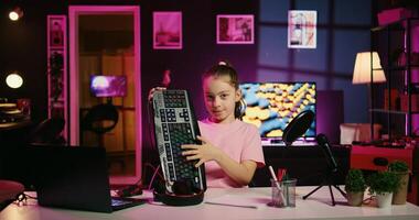Child influencer filming keyboard, mouse and headphones review in home studio, showing capabilities and specifications. Little girl showcasing computer peripherals to fans on gen Z online channel photo