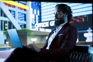 Rich company CEO browses online websites sitting on a bench downtown, checking multinational corporation financial resources. Consultant working on laptop to develop new business branch. photo