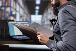 Depot manager checking stock inventory on archived documents, reviewing orders receipts before planning products distribution. Employee working on creating depot labels for import export industry. photo