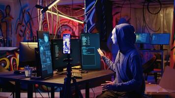 Hackers concealing their identity filming ransom in hidden underground base, threatening to release stolen data publicly if payout demands are not met, using phone to record blackmail footage photo