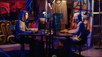 Zoom out shot of malicious men hacking, stealing credit card numbers and manipulating banking systems for their own personal gain. Evil hackers running code in graffiti painted basement photo