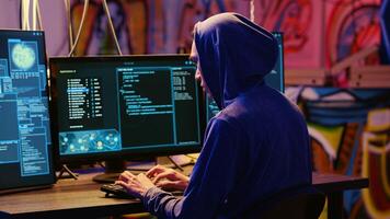 Hacker in graffiti painted hideaway base writing lines of code on computer, developing malware that get past security systems. Rogue programmer uses PC in bunker, running hacking script photo