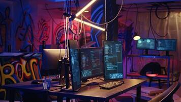 Panning shot of high tech computer system running malicious code in empty basement. PC monitors in empty neon lit criminal hideout used by hackers to commit illegal activities photo