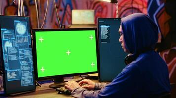 Asian hacker in hidden place with graffiti walls using green screen computer to deploy malware on unsecured devices, stealing sensitive data from unaware users online and selling it on black market photo