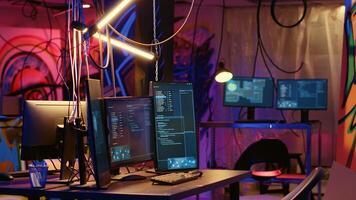 Programming language on PC screens in empty messy hackers base of operations with grunge graffiti drawings sprayed on walls. Neon lit ghetto hideout used by criminals to commit illegal activities photo
