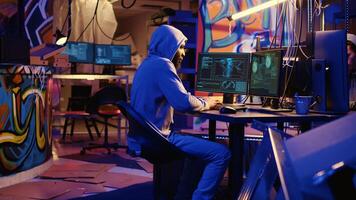 African american hacker doing computer sabotage using encryption trojan ransomware in hidden base. Hooded cybercriminal uses laptop to gain access to victims data in hideaway photo