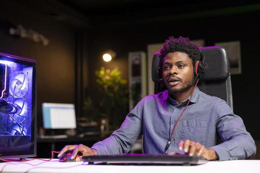 Man playing videogames using computer peripherals, having fun in neon illuminated room. Gamer competing in online multiplayer game on gaming PC, talking with friends through headset photo