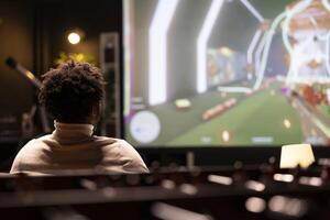 Man seeing videogame gameplay footage on TV uploaded online by pro streamer. BIPOC gamer sitting at home enjoying time off from work looking up game info before deciding to buy it photo