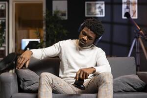 African american man taking a break after playing videogames in apartment all day. Gamer setting controller down, taking time out from participating in PvP online multiplayer game using console system photo