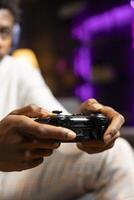 Close up shot of gamepad controller in BIPOC man hands playing intense online videogame in neon illuminated living room. Gamer participating in internet esports competition, playing on gaming console photo