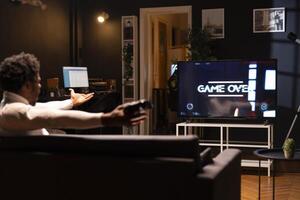 Gamer feeling gutted after losing SF videogame level, screaming at television set in anger. Angry man at home yelling, frustrated after seeing game over screen on smart TV display photo