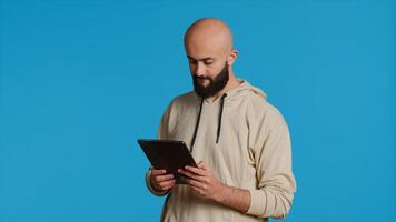 Arab guy using tablet to scroll on online websites, looking for something on the internet and using social media apps. Modern person working with touchscreen device in studio. Camera 1. photo