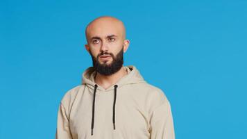 Young guy gesturing no sign over studio background, posing in studio and showing negative emotion. Middle eastern model doing forbidden gesture, expressing his refusal. Camera 2. Handheld shot. photo