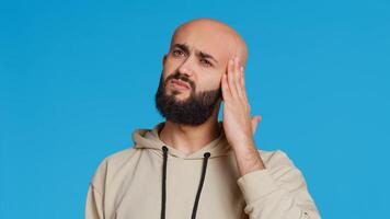 Unwell arab model dealing with serious headache in studio, feeling sick with a painful migraine and rubbing temples to ease the pressure. Tired person suffering from pain and tension. Camera 2. photo