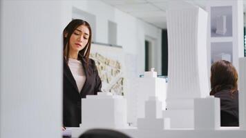 At design table, engineer reviews schematics and 3D construction plans in order to develop manufacturing layout for urban housing project. Woman evaluates sizes and components. Handheld shot. photo