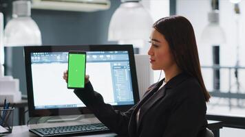 Developer shows mobile phone with greenscreen template, working in small business coworking space. Engineer using isolated copyspace layout on blank mockup screen, chromakey background. photo