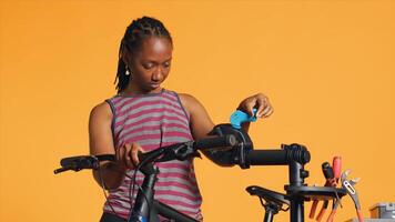 African american woman setting up bike repair stand, using it to adjust derailleur, fixing broken wheels, studio background. Professional placing bicycle on workstand to do checkup on it, camera A photo