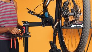 African american mechanic utilizing different tools to repair damaged bike handlebar grips, studio background. Employee using specialized gear to fix shifters and brake levers on bicycle, camera A photo