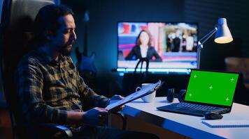 Teleworking financial advisor analyzing statistical charts on documents in front of green screen laptop in living room. Remote worker checking business paperwork, looking at mockup notebook photo