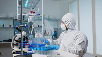 Biologist doctor in ppe suit checking liquid sample typing on pc in equipped laboratory. Team examining vaccine evolution in medical lab using high tech and chemistry tools for scientific research photo