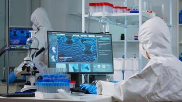 Chemist in ppe suit typing on computer checking virus development in modern equipped laboratory. Doctor working with various bacteria, tissue and blood samples, pharmaceutical research for antibiotics photo