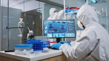 Chemist man in coverall typing on computer analysing vaccine evolution in modern equipped laboratory. Team of doctors in ppe suit using high tech for researching treatment against covid19 virus photo