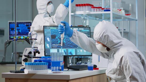 Research scientist in protection suit using micropipette filling test tubes in lab. Team of microbiologists examining virus evolution using high tech analysing treatment development against covid19. photo