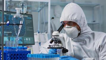 Close up of scientist looking through a microscope wearing ppe suit in equipped lab. Team examining virus evolution using high tech for scientific research of vaccine development against covid19. photo