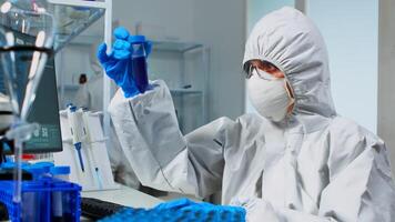 Researcher in coverall testing liquid sample using test tubes for new treatment medical laboratory. Team of doctors examining virus evolution using high tech for vaccine development against covid19 photo