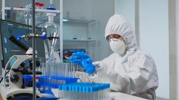 Lab technician in coverall examining samples of liquid typing on computer results sitting in equipped laboratory. Scientist working with various bacteria tissue pharmaceutical research for antibiotics photo