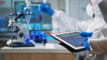 Back view of scientist in coverall analyzing virus evolution looking on digital tablet. Team of microbiologists conducting vaccine development using high tech for researching treatment against covid19 photo