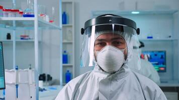 Portrait of tired scientist man looking at camera wearing protection suit in equipped lab. Examining virus evolution using high tech and chemistry tools for scientific research, vaccine development photo
