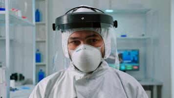 Portrait of chemist doctor looking up at camera sitting in modern equipped lab wearing protection suit. Examining virus evolution using high tech and chemistry tools for vaccine development. photo