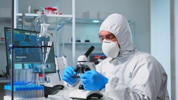 Scientist in ppe suit placing a slide on specimen stage of a laboratory microscope making adjustments. Chemist in coverall working with various bacteria, tissue blood samples for antibiotics research photo