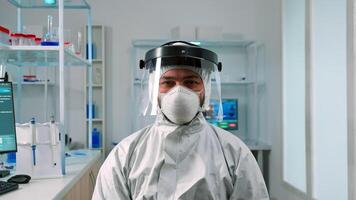 Man scientist in ppe suit looking exhausted at camera in modern equipped lab. Overworked team examining virus evolution using high tech and chemistry tools for scientific research, vaccine development photo
