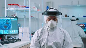 Doctor man looking at camera sitting in scientific equipped lab dressed in protection suit against coronavirus. Examining virus evolution using high tech, chemistry tools for vaccine development. photo