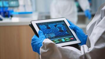 Back view of doctor in protection suit analyzing virus evolution looking on digital tablet. Team of scientists conducting vaccine development using high tech for researching treatment against covid19 photo