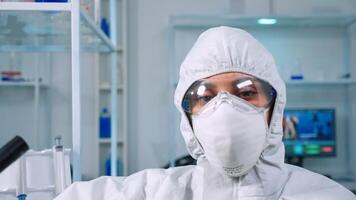 Tired doctor wearing coverall looking exhausted at camera in modern equipped lab. Scientist examining virus evolution using high tech and chemistry tools for scientific research, vaccine development. photo