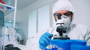 Laboratory scientist in ppe suit conducting experiment looking through a microscope in modern lab. Man working with various bacteria tissue, blood samples, concept of medical research for antibiotics photo