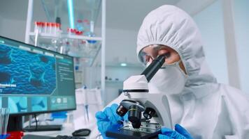 Chemist researcher wearing coverall in sterile lab doing experiments for medical industry using microscope. Doctors examining virus evolution using high tech for vaccine development against covid19 photo
