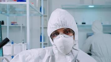 Portrait of tired scientist in coverall looking at camera sitting in modern equipped laboratory. Team of doctors examining virus evolution using high tech and chemistry tools for vaccine development. photo
