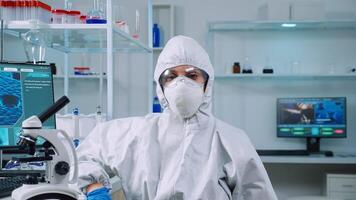Tired microbiologist in coverall sitting in laboratory looking at camera. Team of scientits examining virus evolution using high tech and chemistry tools for scientific research, vaccine development. photo