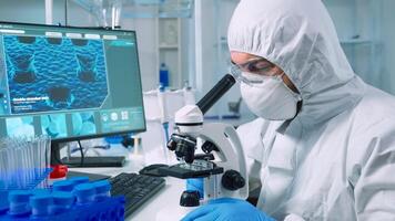 Medical research scientist in coverall conducting vaccine development under digital microscope in a biological applied science laboratory. Lab engineer in ppe suit working on medical treatment photo