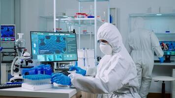 Doctor with protection suit working with blood samples in laboratory typing on computer. Chemist examining vaccine evolution using high tech for research in treatment development against covid19 virus photo