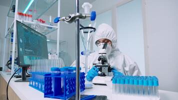 Scientist microbiology lab in protective suit conducting virus analysis looking through microscope. Team of doctors examining virus evolution using high tech for vaccine development against covid19 photo