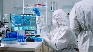 Scientist nurse in ppe suit taking notes on computer looking at test tube in laboratory. Chemists examining vaccine evolution using high tech for research in treatment development against covid19 virus photo