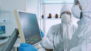 Chemists in protection suit discussing about changes in vaccine composition in equipped lab pointing desktop. Doctors examining virus evolution using high tech researching diagnosis against covid19 photo